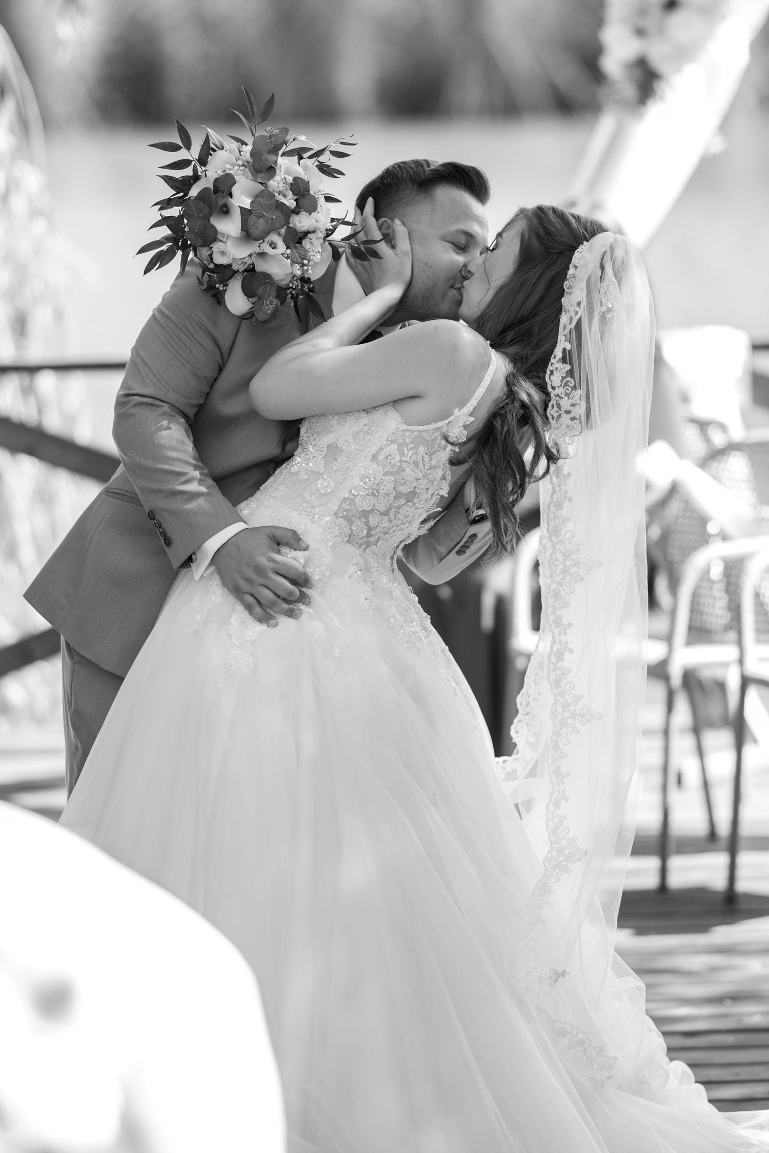 A romantic wedding kiss captured in black and white during an outdoor ceremony.