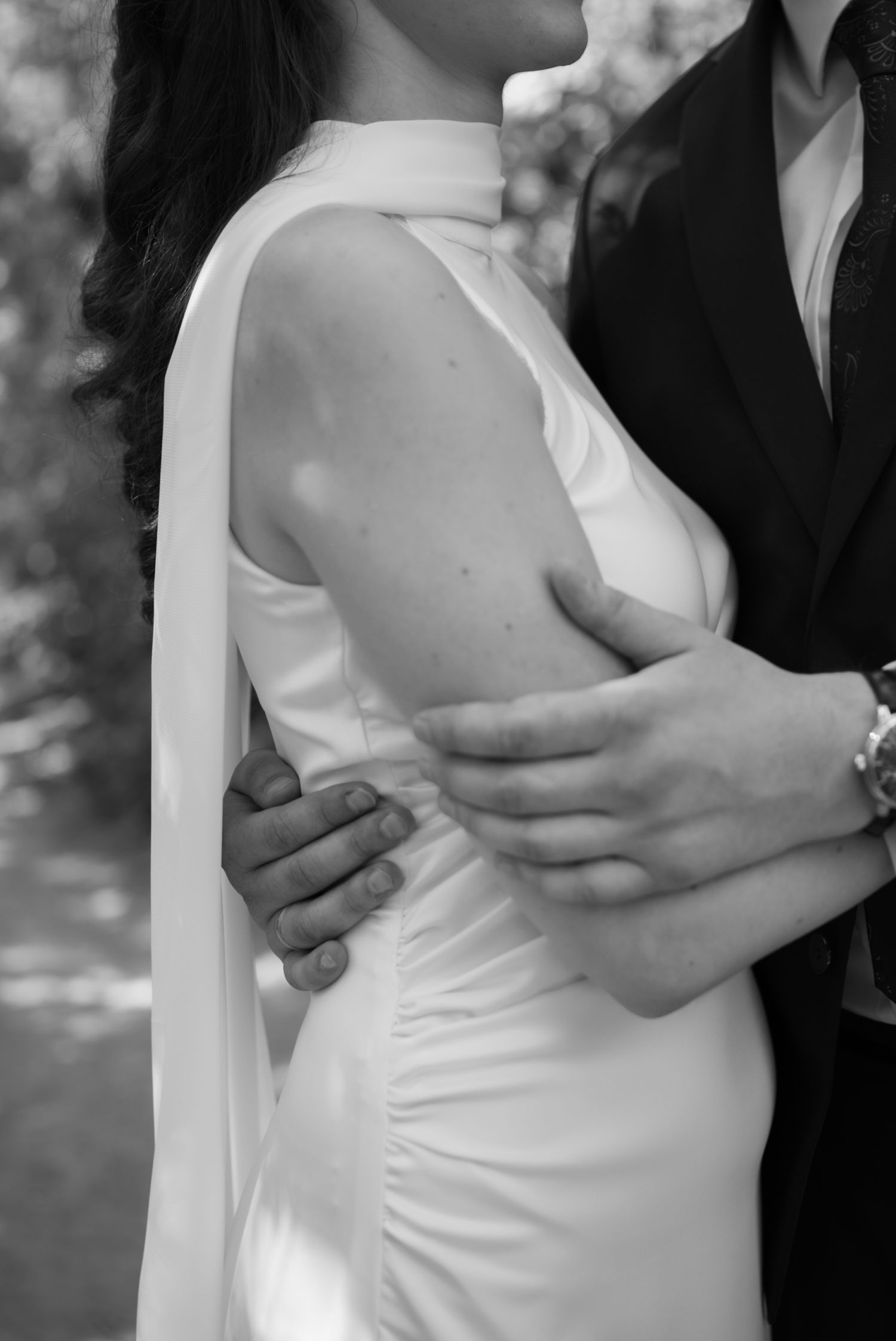 Black and white photo of a couple embracing, bride in elegant white gown with cape detail, groom in dark suit.