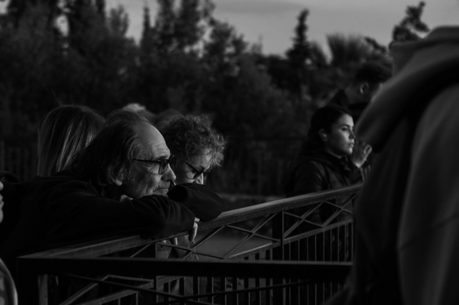 Black and white photo of spectators watching from behind a railing at dusk.