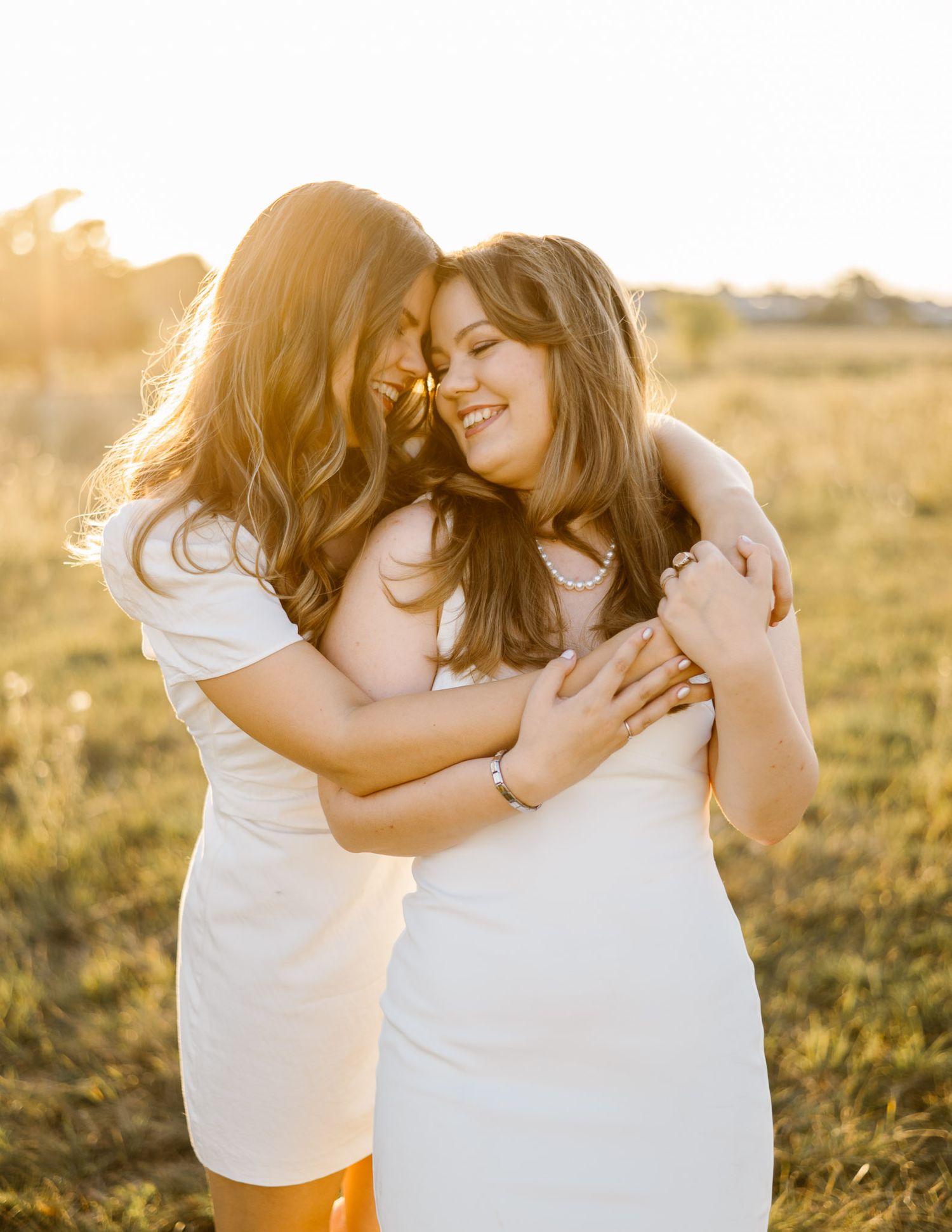 Friends in white outfits embracing and laughing together in golden sunlight.
