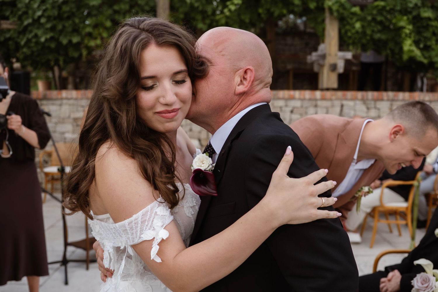 Emotional father-daughter dance embrace at outdoor wedding reception with guests in background.