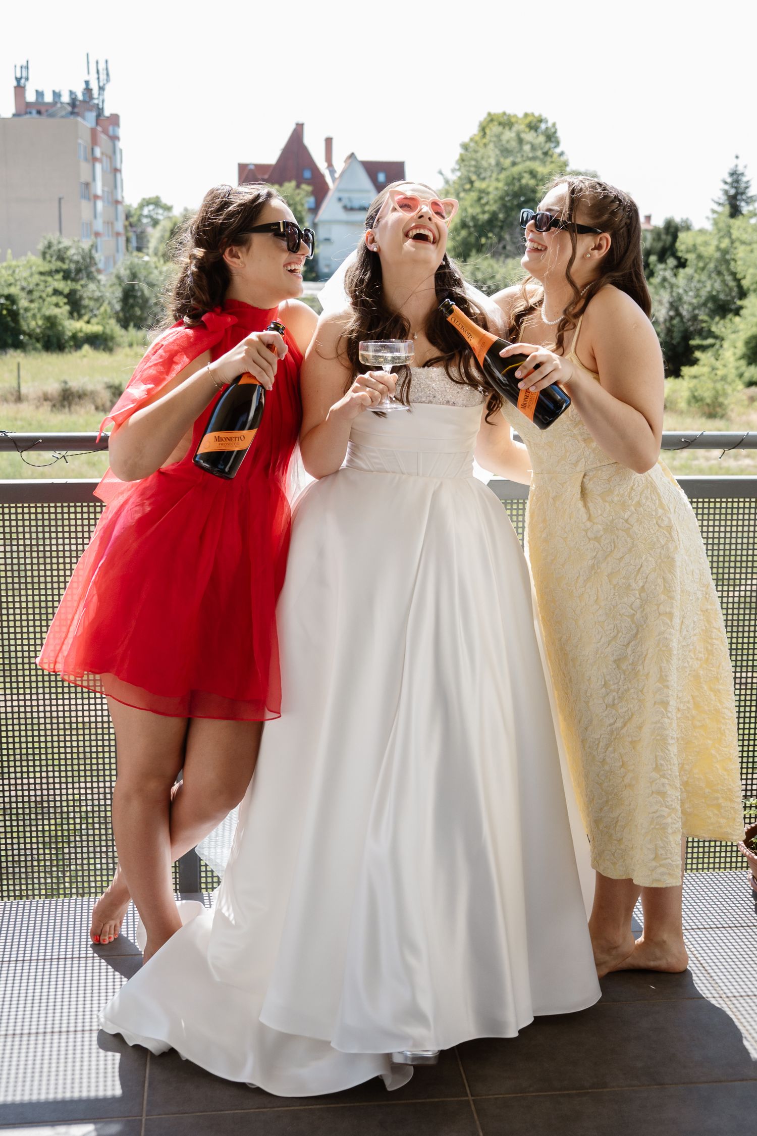 Wedding party in red and white dresses posing playfully on an outdoor balcony.