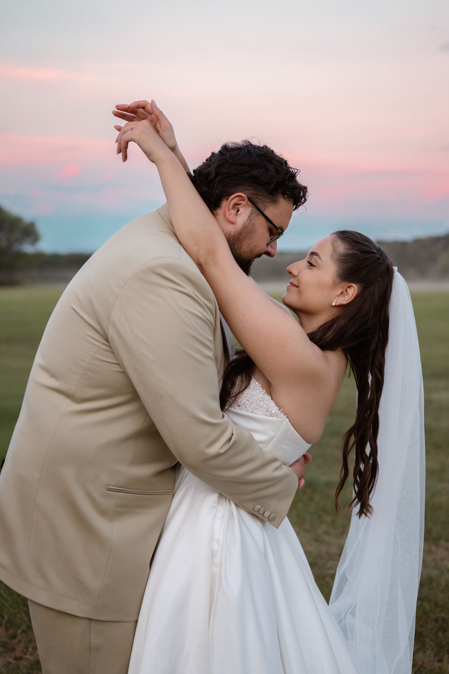 A couple dancing together in a field during sunset.