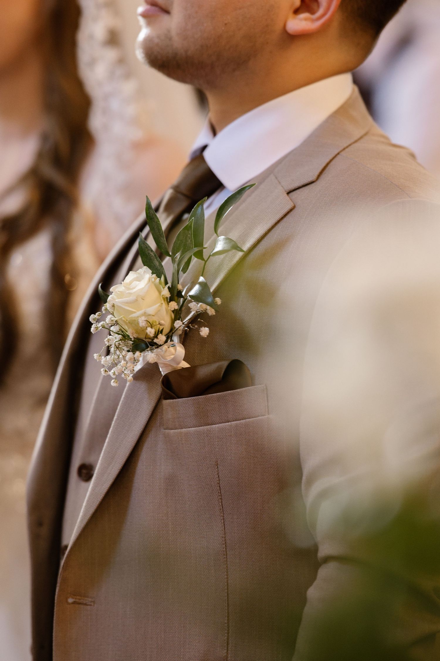 Groom wearing a brown suit with a white boutonniere and floral accent.