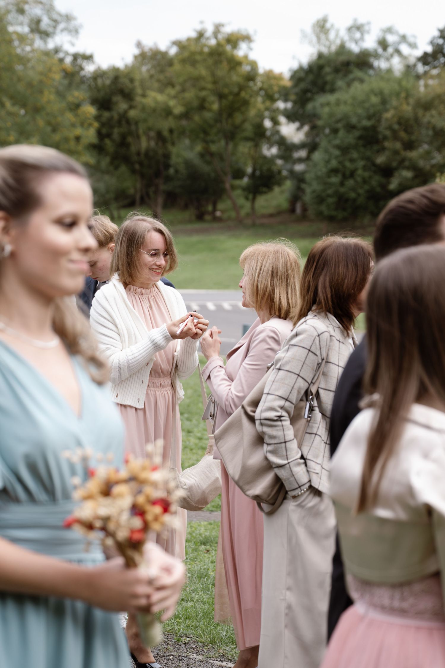 Wedding guests in pastel dresses gather outdoors during a reception.