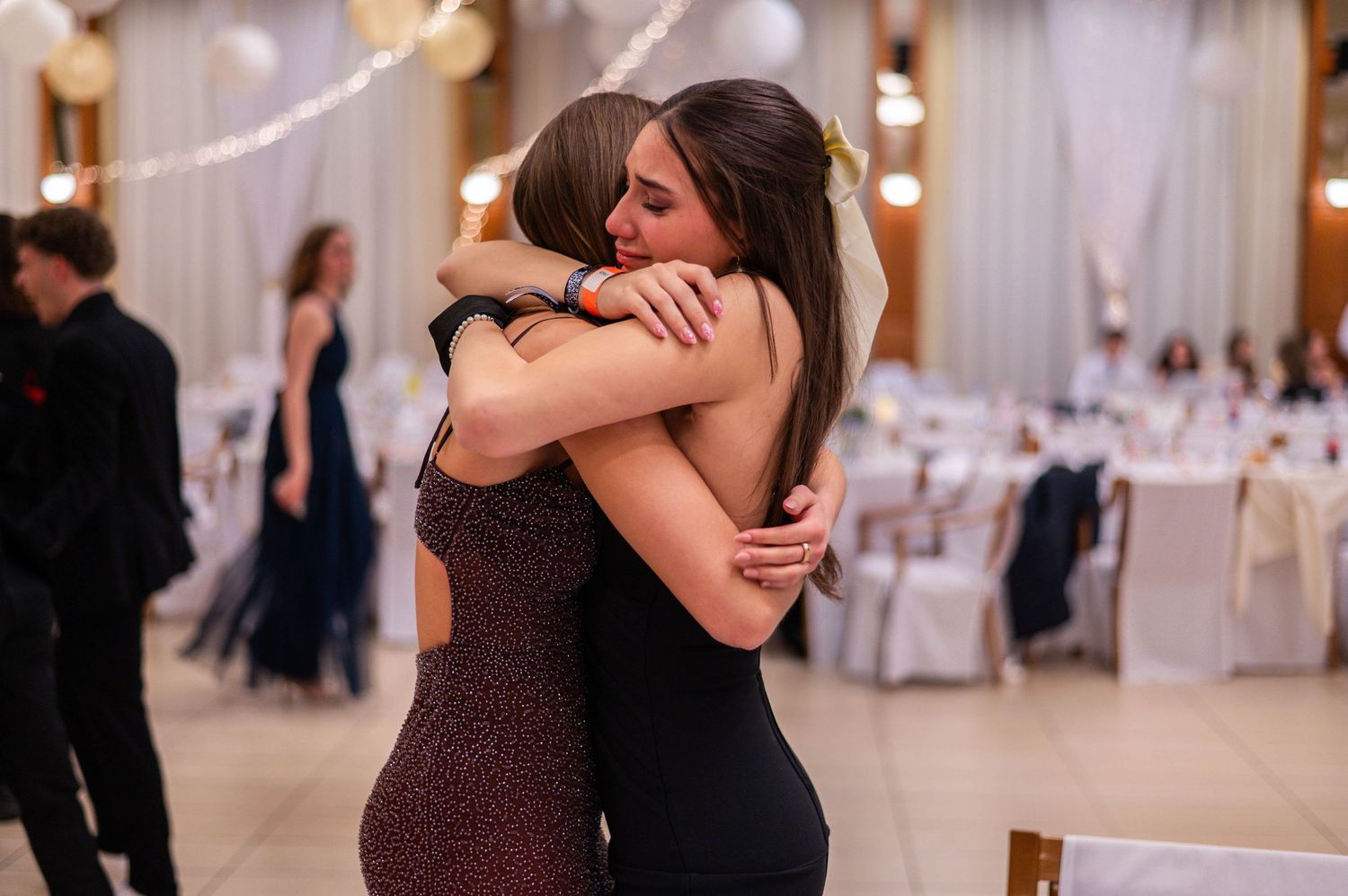 Emotional embraces and dance moments at a wedding reception with white decor and string lights.