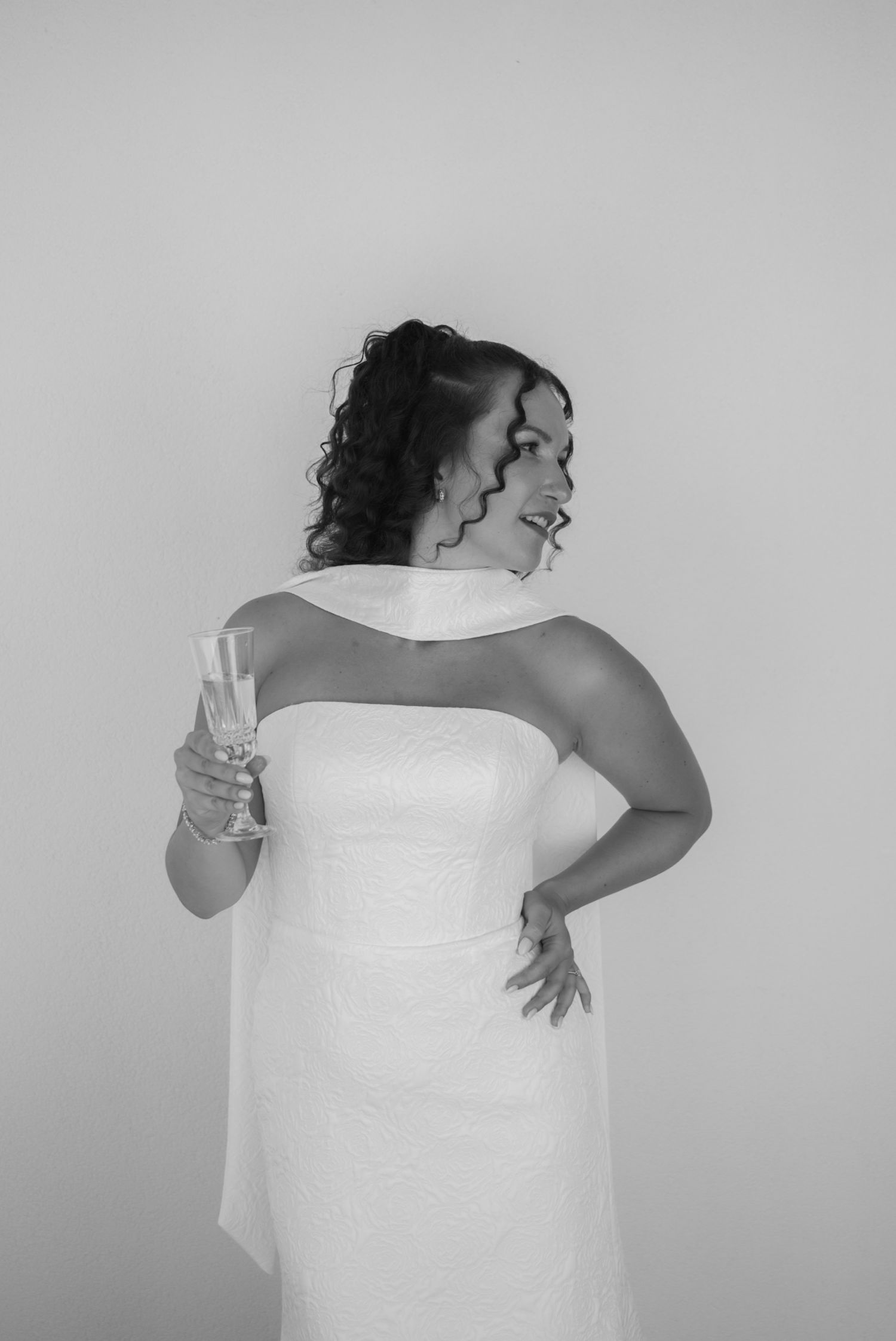 Elegant bride in white strapless gown holding champagne glass, posing in black and white portrait.