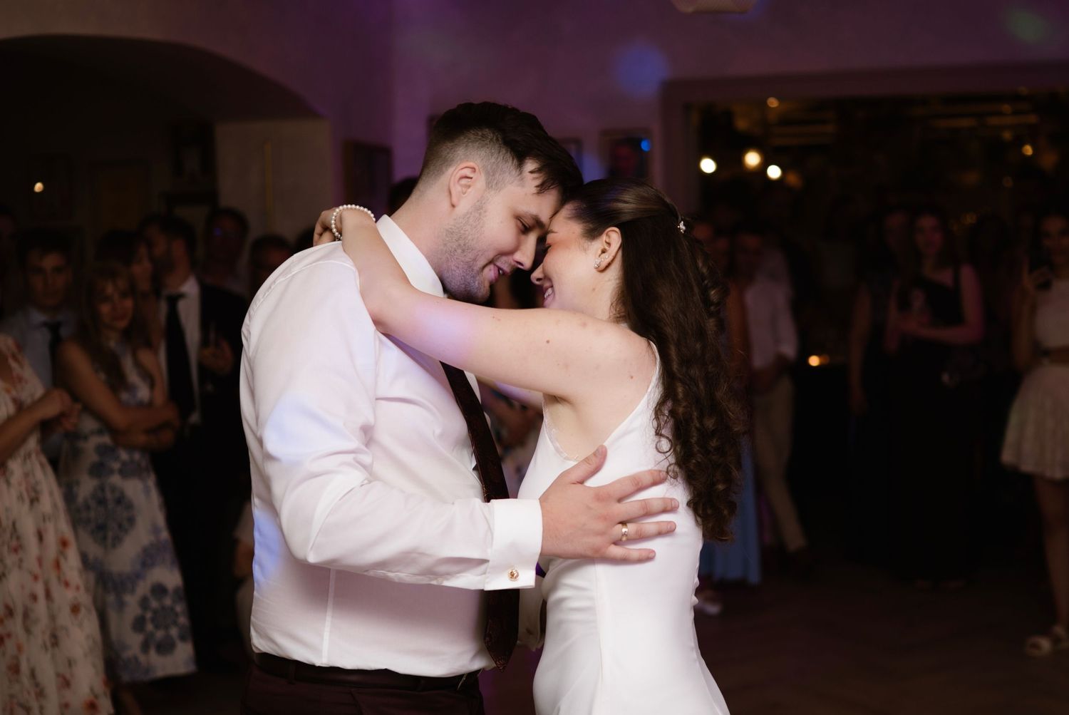 Bride and groom sharing intimate first dance embrace surrounded by wedding guests.