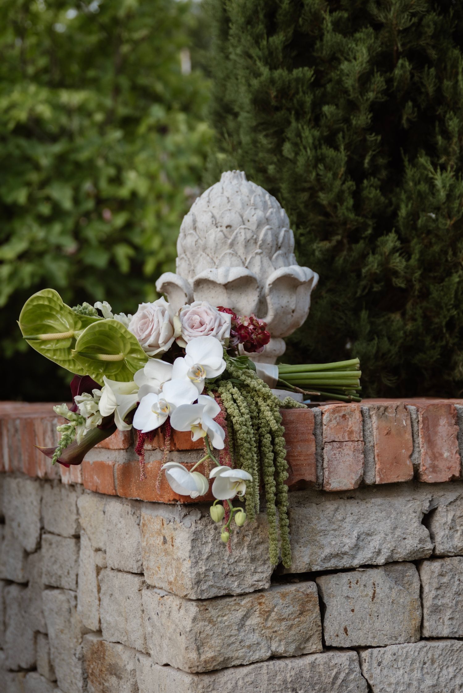 Elegant wedding bouquet with white orchids and roses resting on a rustic stone wall.