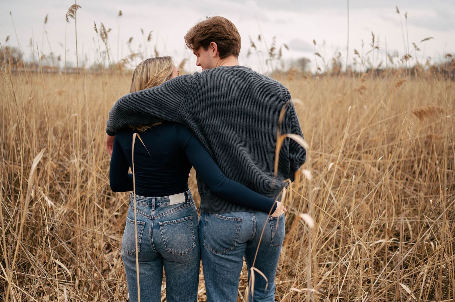 Back view of a couple walking together through a golden field at sunset.