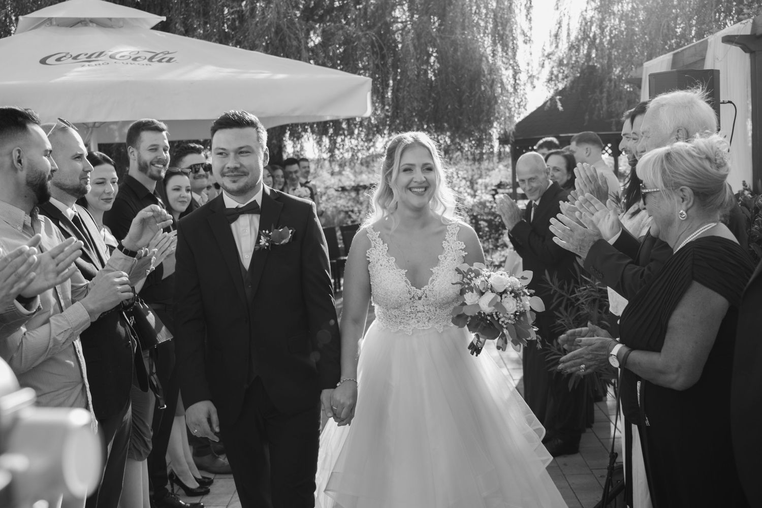 Wedding guests gather under trees for an outdoor celebration with joyful expressions.