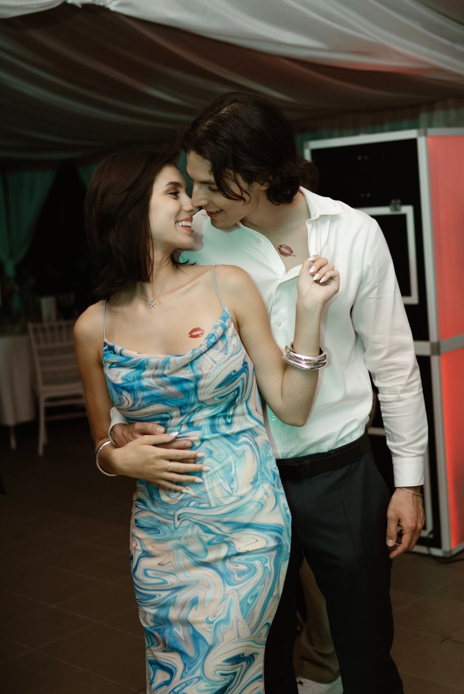 A couple shares a romantic dance at a wedding reception, the woman wearing a blue marble print dress.