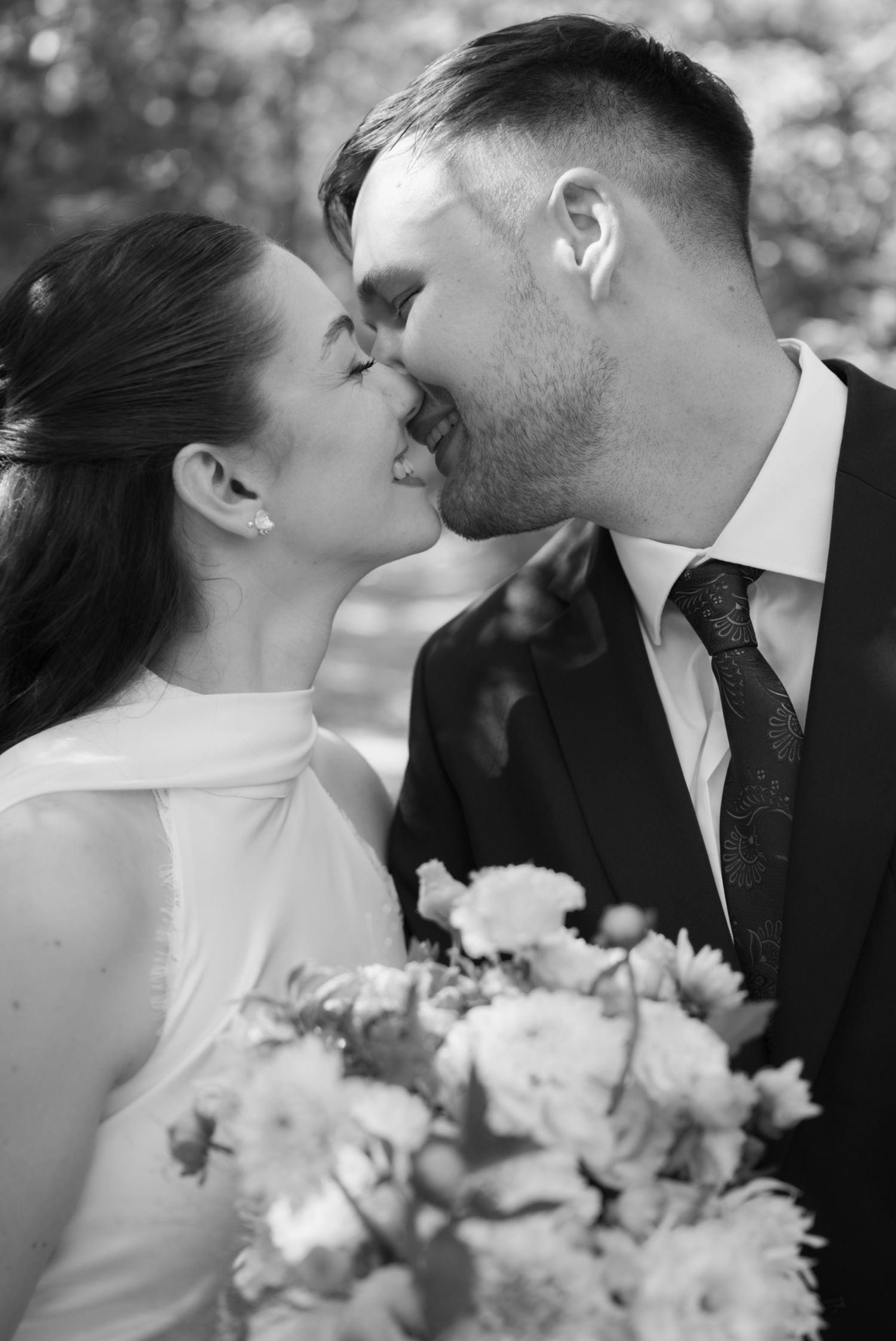 Black and white photo of a bride and groom sharing a kiss, bride holding a bouquet of flowers on their wedding day.