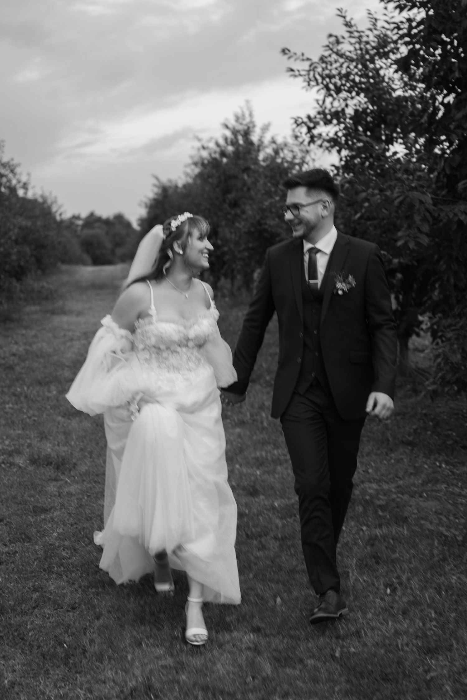 Black and white wedding photos showing playful moments between newlyweds walking outdoors.