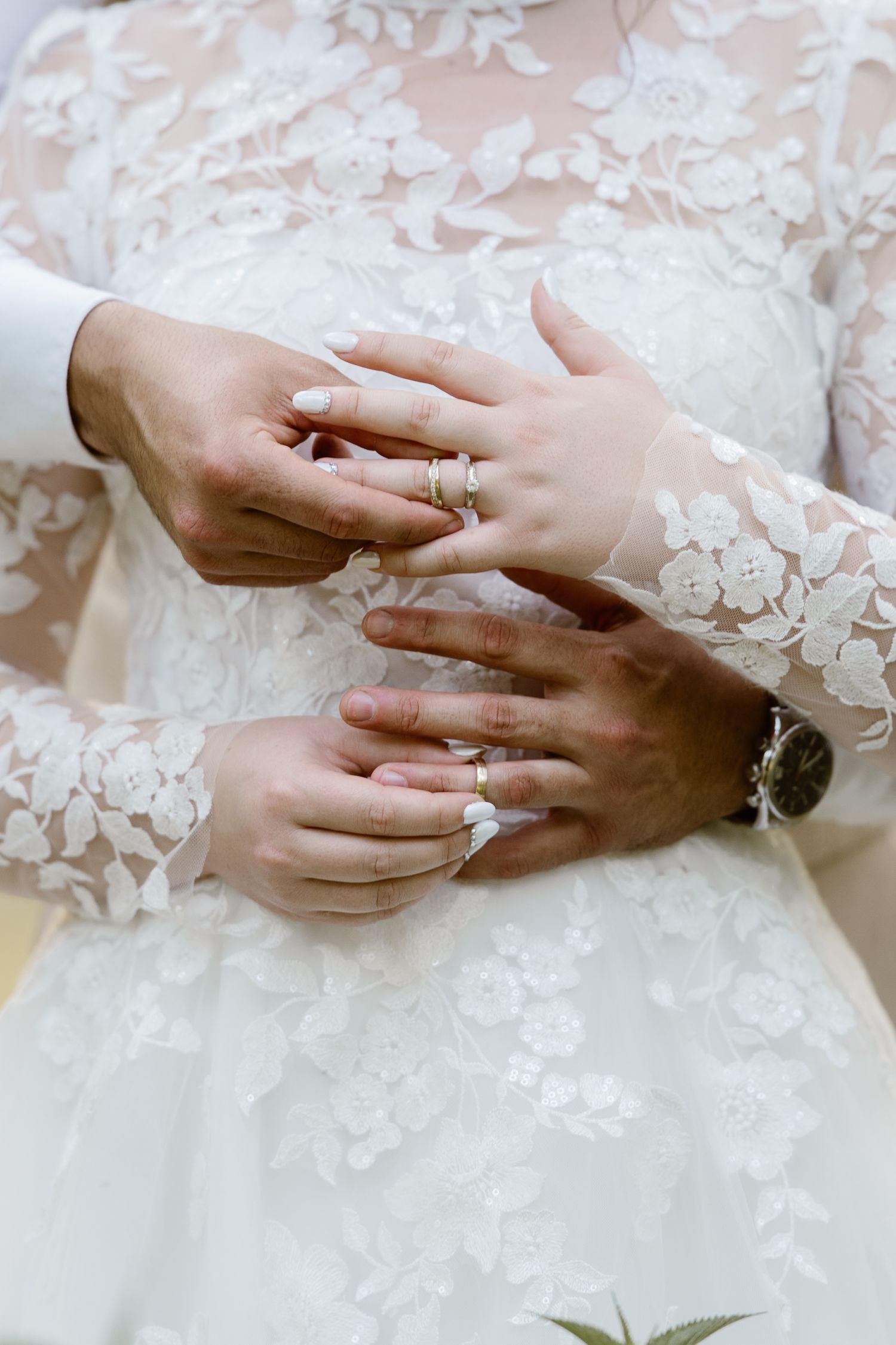 Close-up shots of hands exchanging wedding rings on a lace dress.