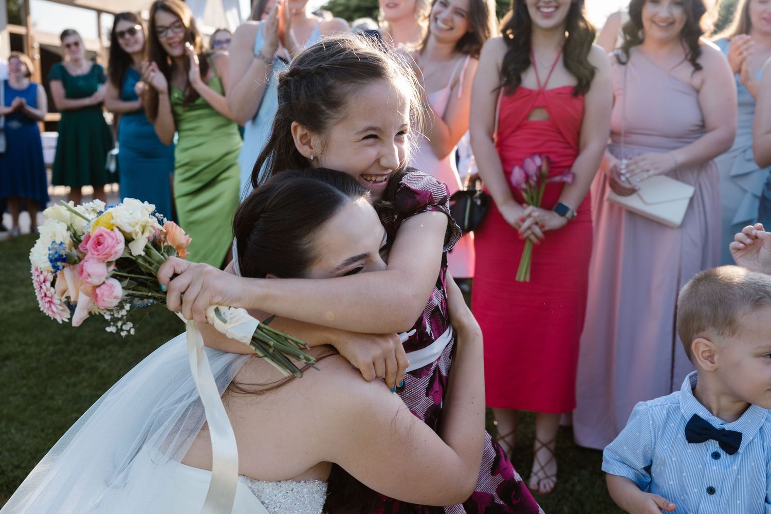 Wedding party members in light colored dresses and suits gather outdoors for group photos.