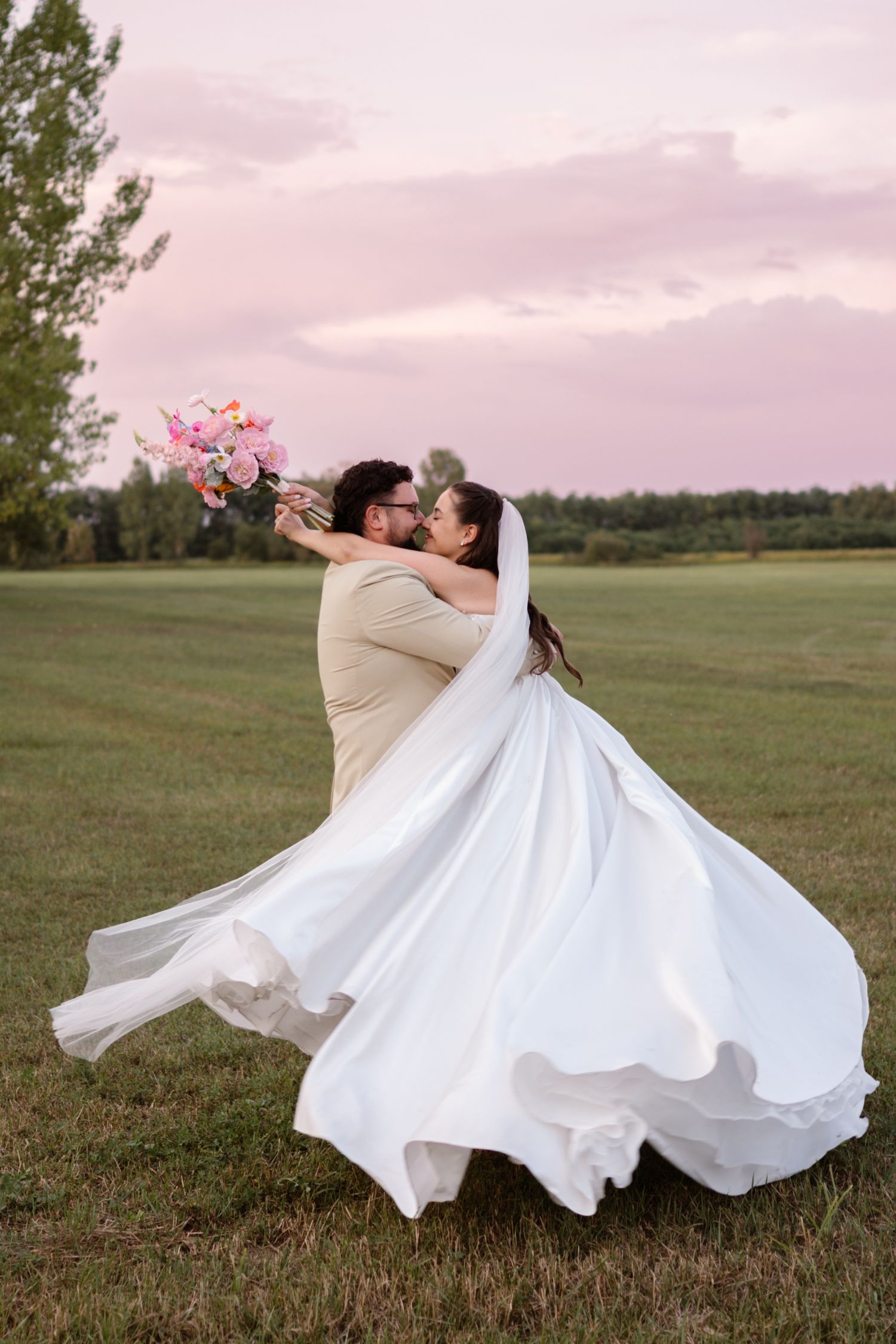 Wedding dress twirls dramatically across open field during sunset photoshoot.