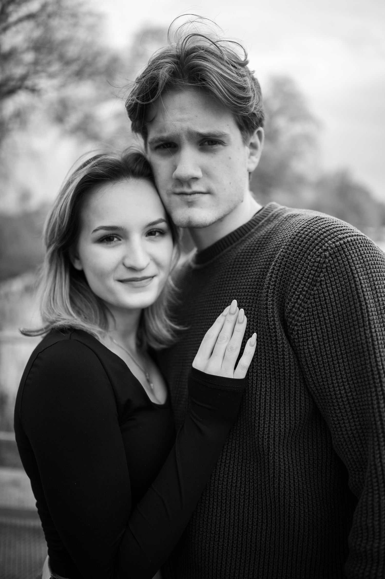 A romantic black and white portrait series showing a couple in casual attire embracing outdoors.
