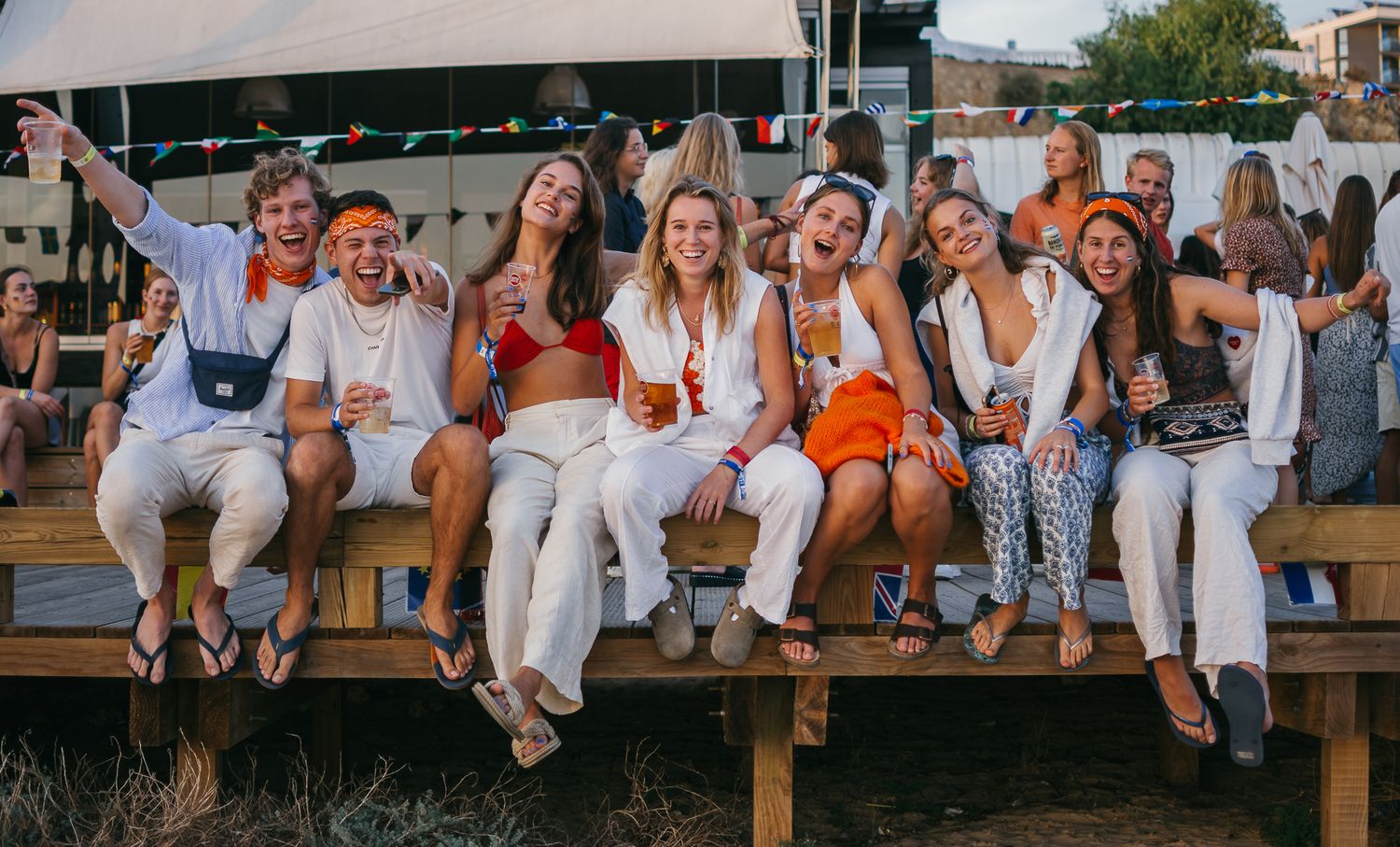Large group of people posing together on wooden deck at sunset.