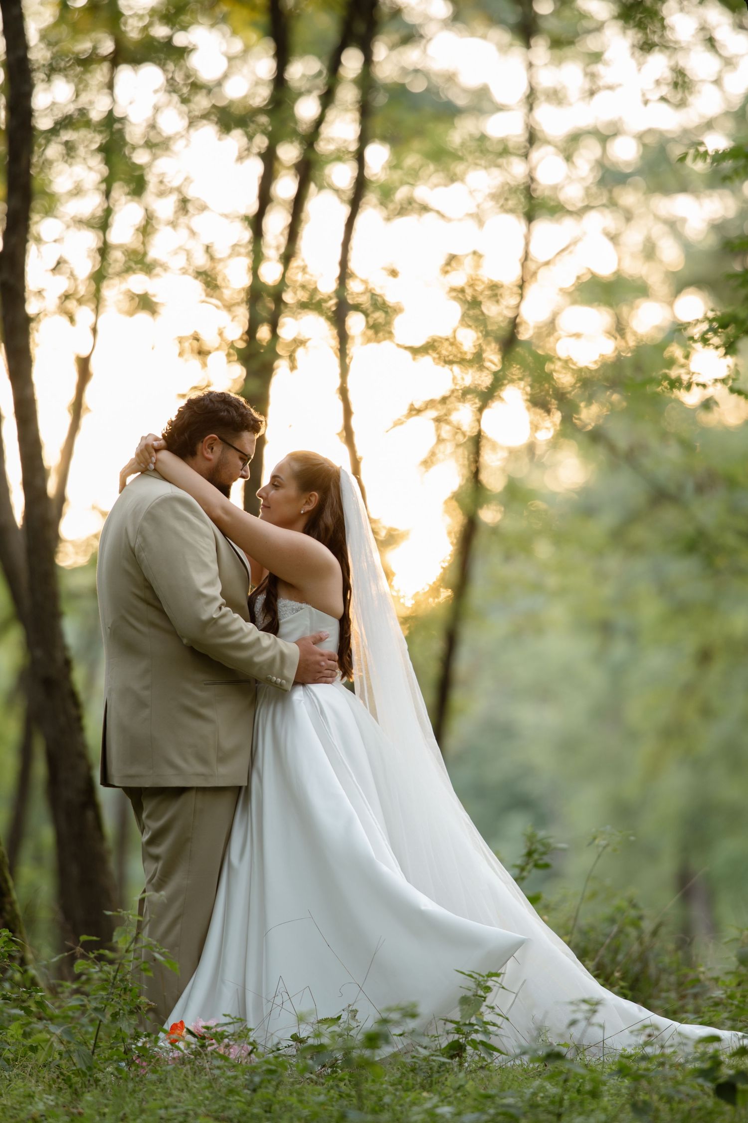 A tender moment between newlyweds in a wooded area during golden hour.