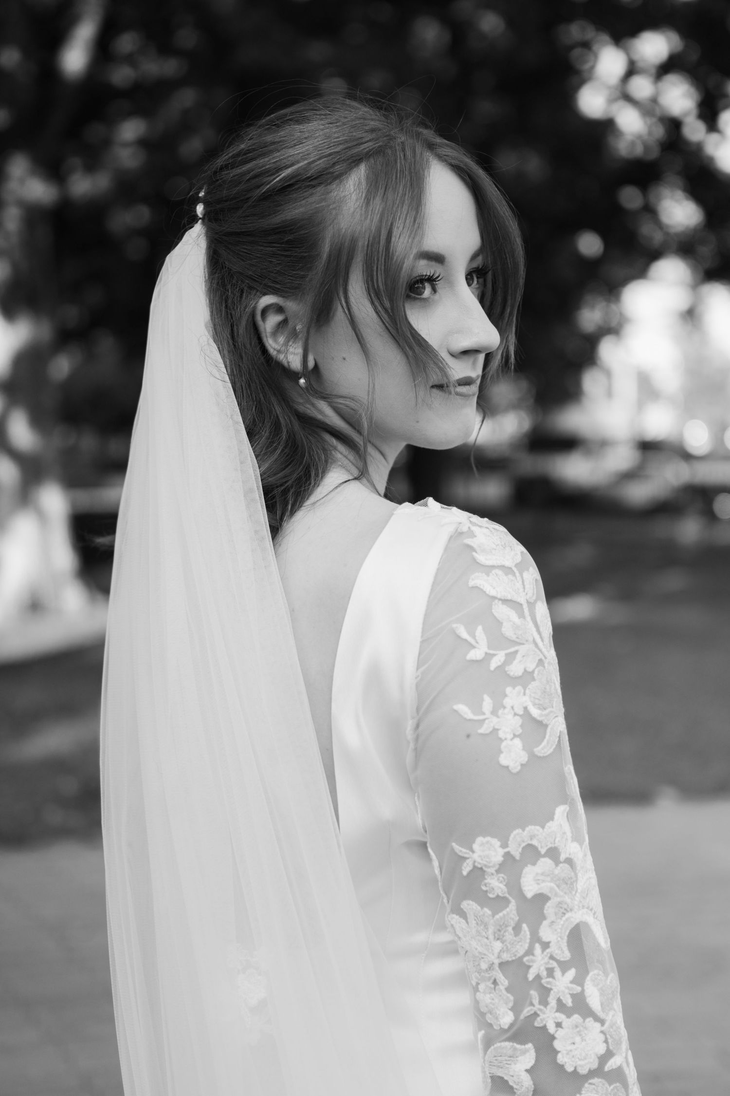 An elegant bride in a lace-sleeved wedding dress and veil looking over her shoulder.