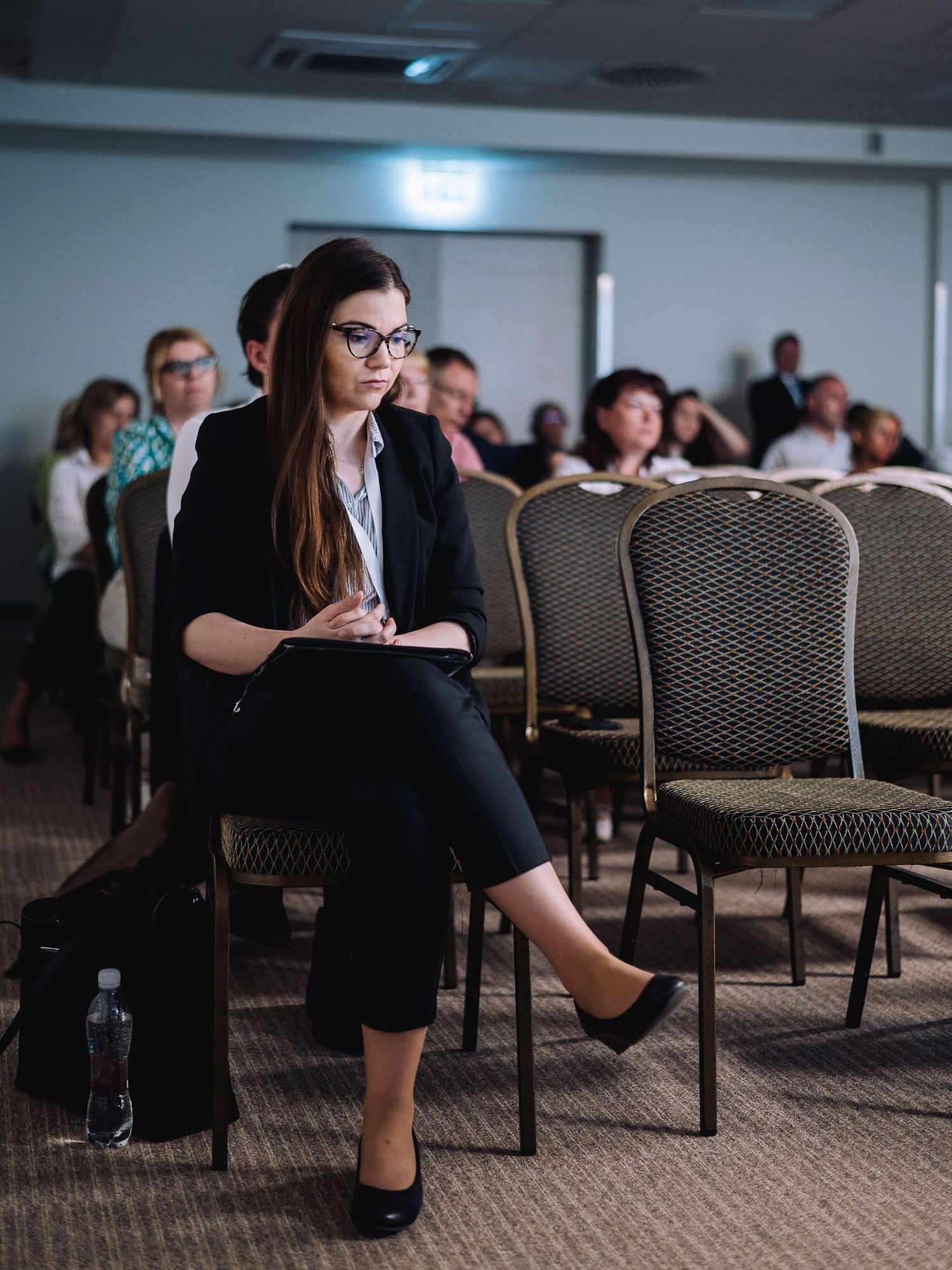 Conference attendees seated in rows of patterned chairs during a professional event.