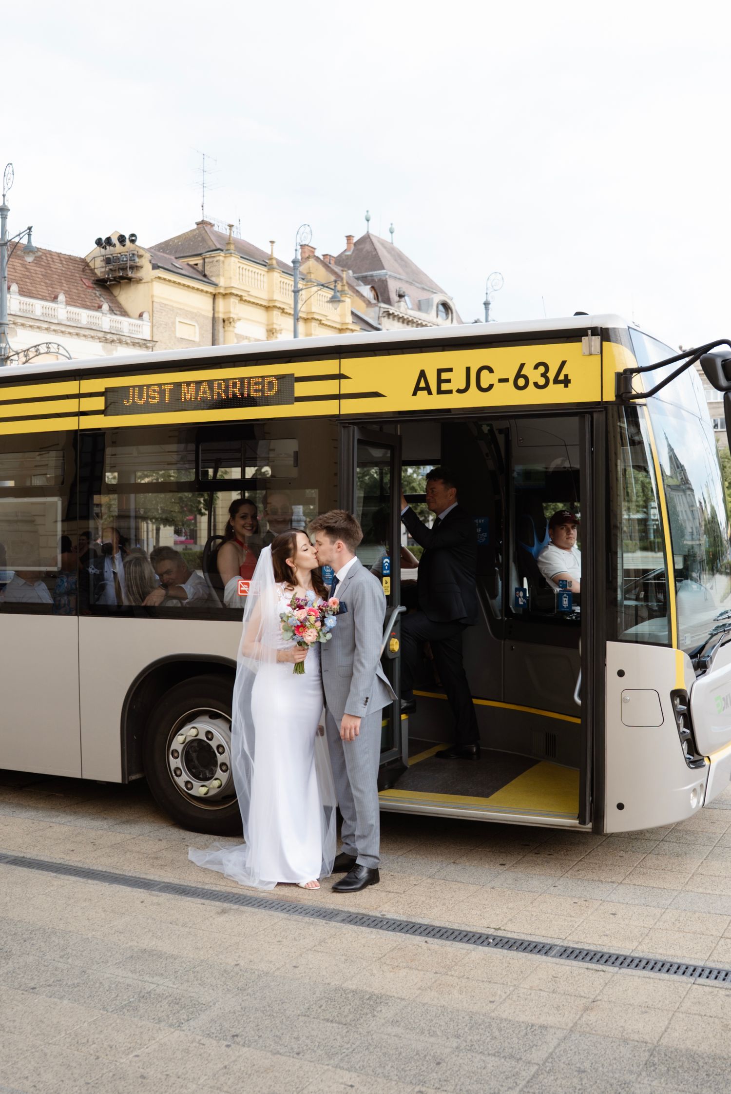 Newlyweds kissing in front of a yellow Just Married bus outside after their wedding ceremony.