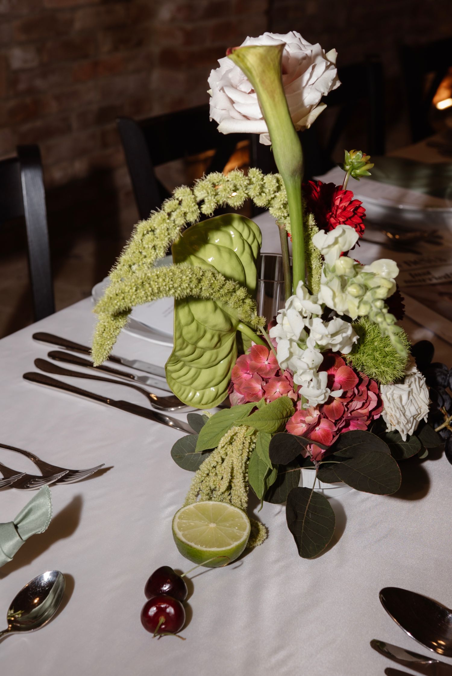 Elegant wedding table centerpiece with calla lily, roses, hydrangeas, lime, and lush greenery on white linen.