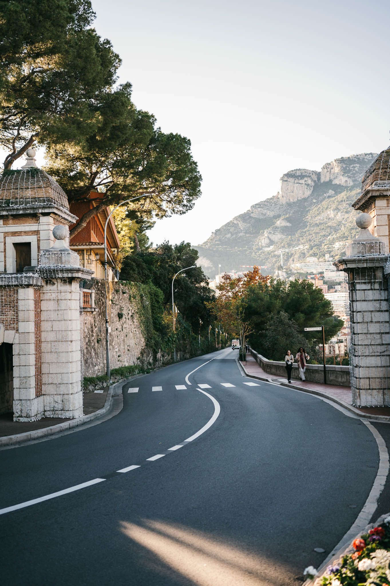 Scenic winding mountain road with stone pillars and gates along the Mediterranean coast during golden hour.