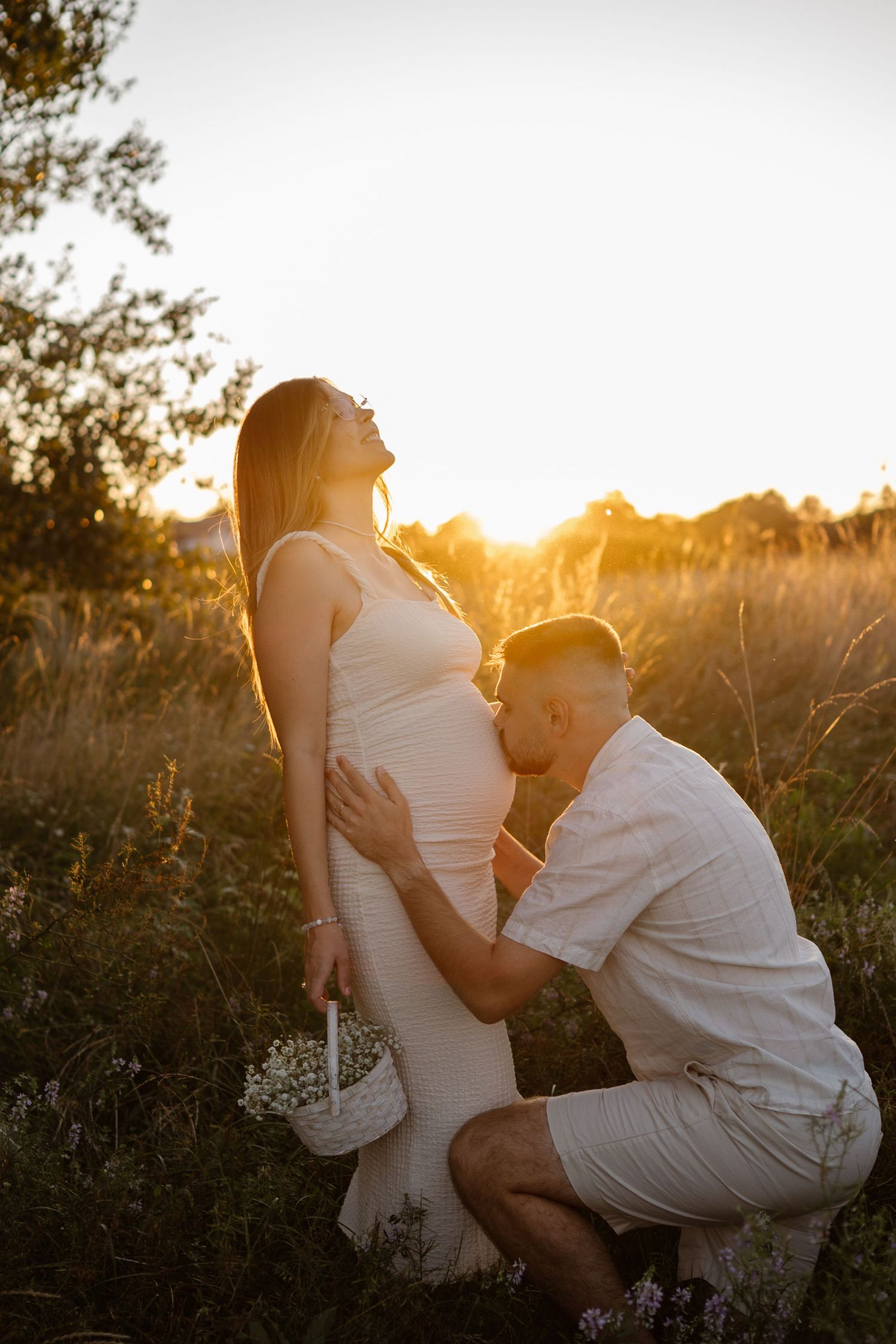 Romantic sunset maternity photoshoot in a field with golden hour lighting.
