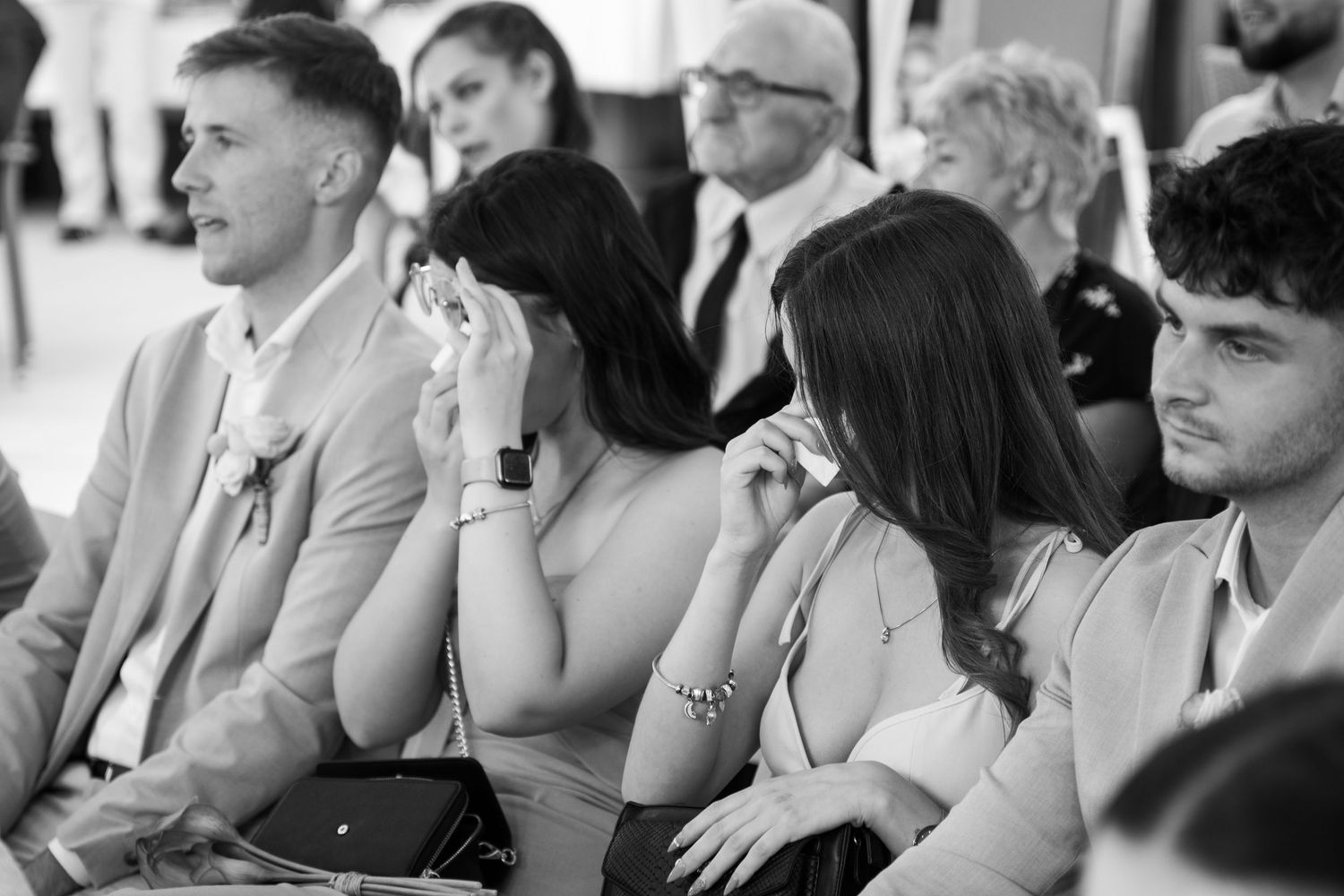Wedding guests seated outdoors watching ceremony with emotional expressions.