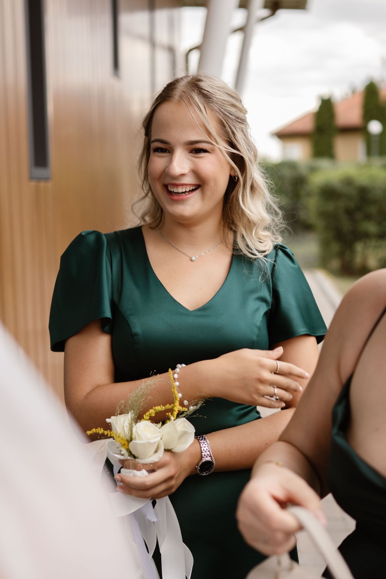 A bridesmaid in an emerald green dress holding a white floral corsage.