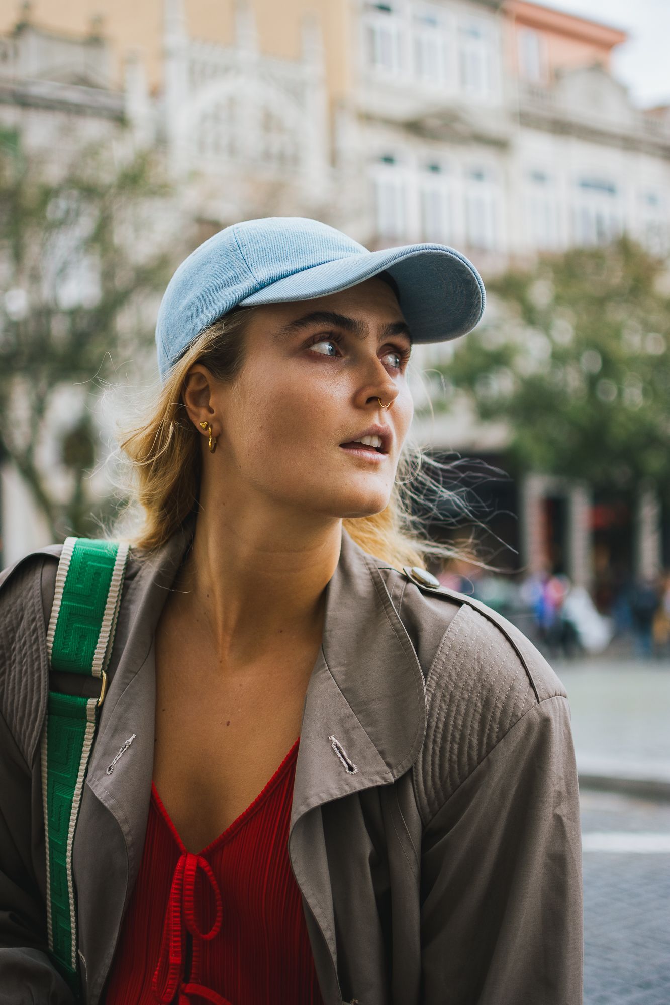 Person wearing a baseball cap and brown jacket looking to the side on a city street.