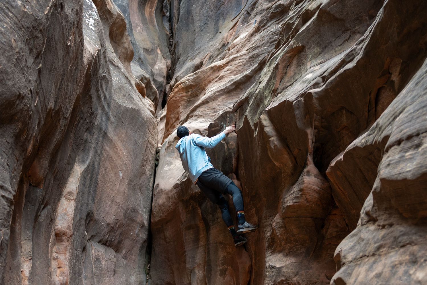 Man climbs rock wall in an Utah slot cavern.