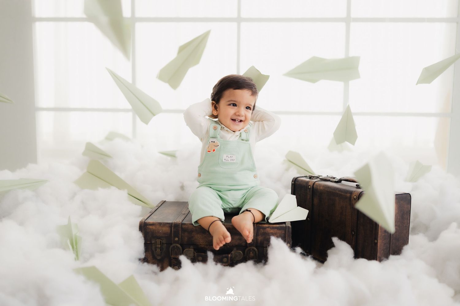 Paper airplanes float around a vintage travel-themed baby photo setup.