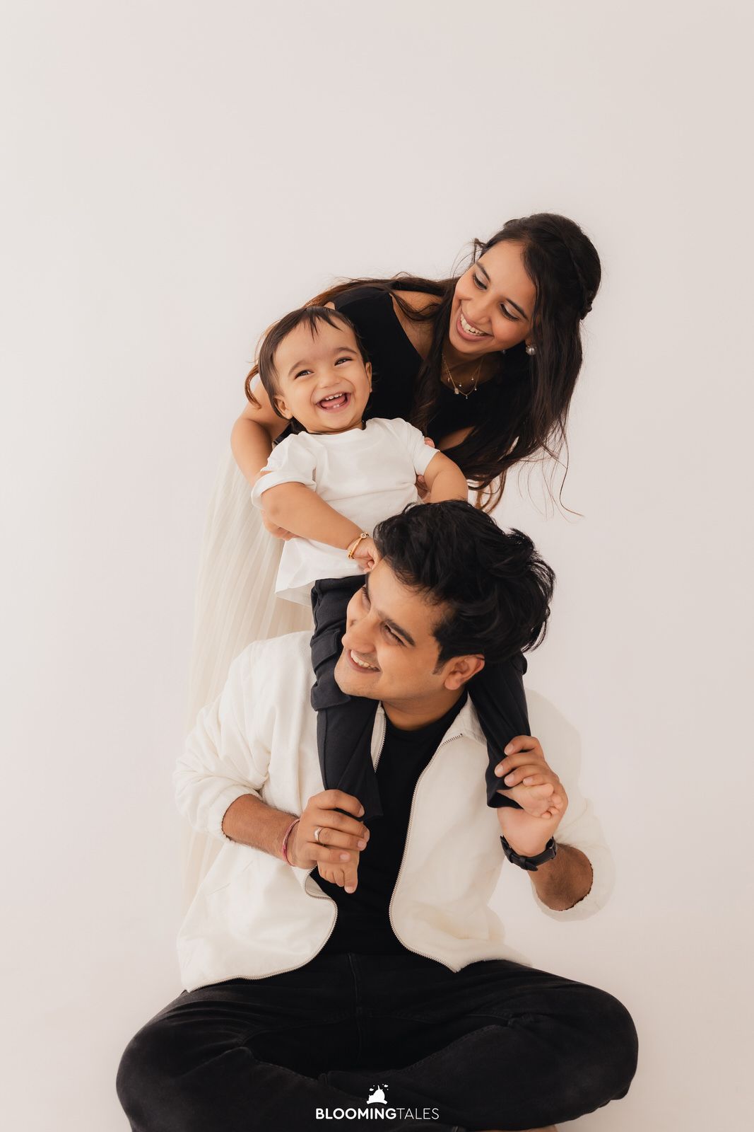 Family portrait with parents and child in coordinated black and white outfits against white background.