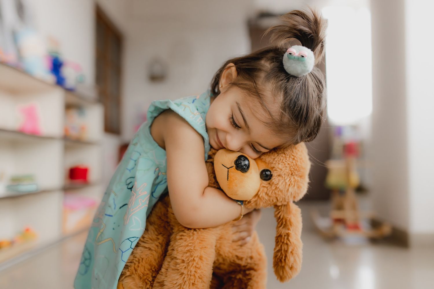 Child in turquoise dress sleeping while hugging a brown teddy bear.