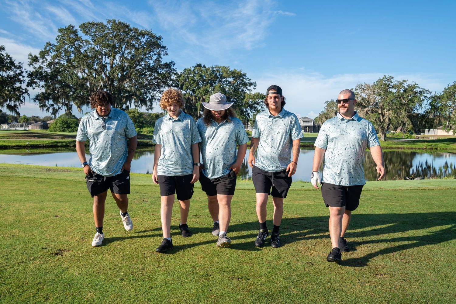 A group walking together on a sunny golf course with trees and a water feature in the background.