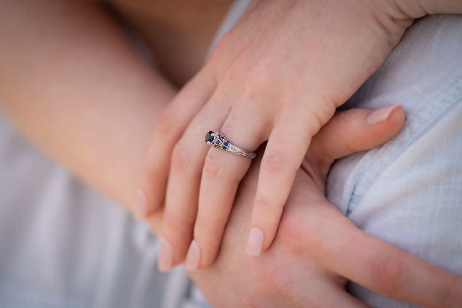 Close-up detail of an engagement ring on a hand against a soft background.