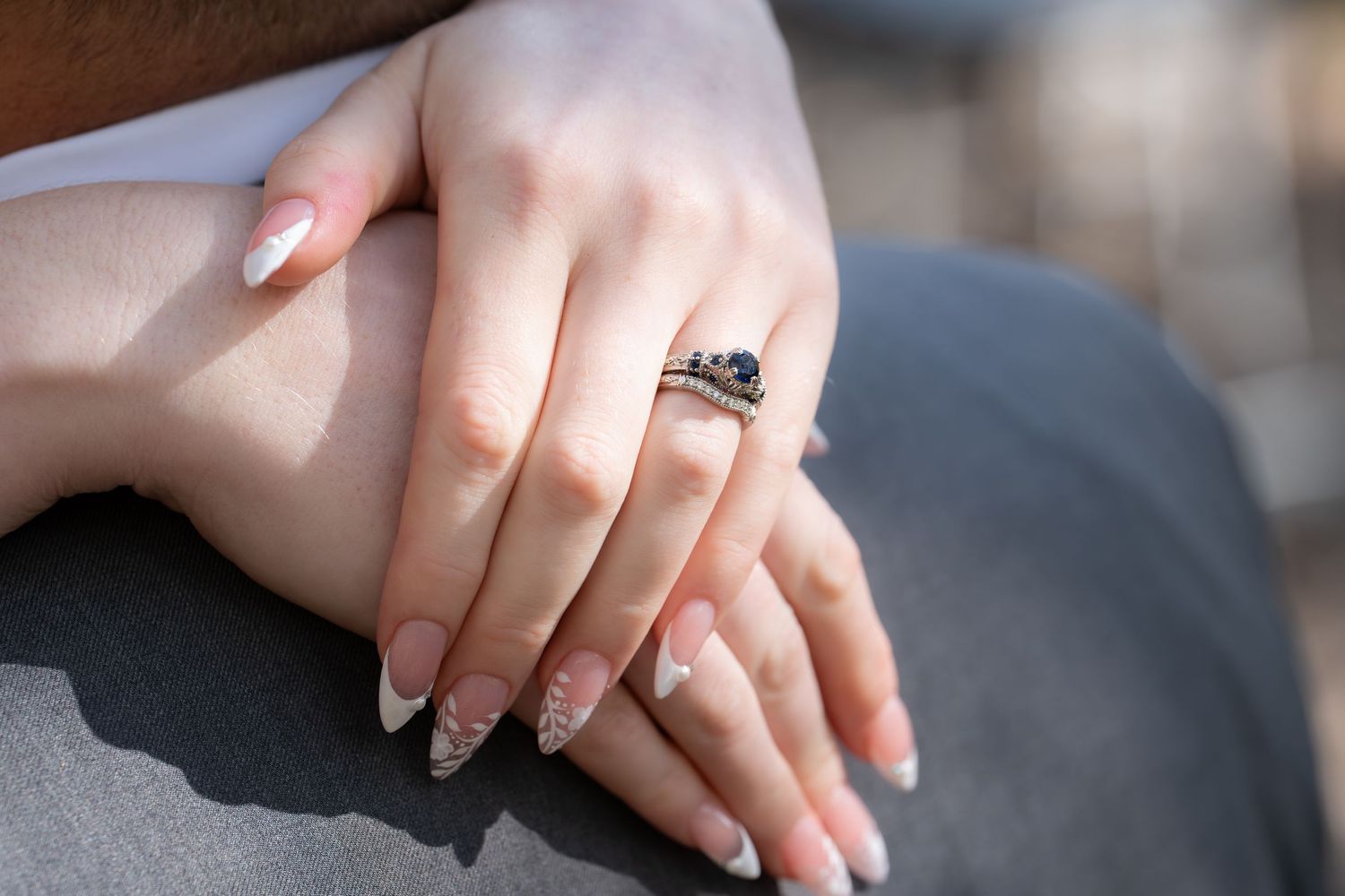 Close-up view of hands wearing engagement ring and wedding band on a gray background.