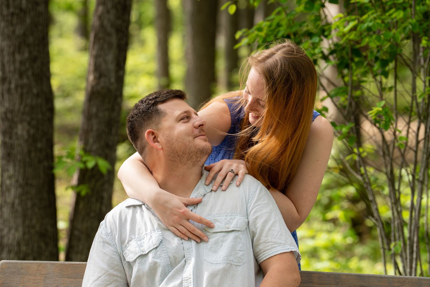 Intimate engagement photo of a couple surrounded by green spring trees and natural light.