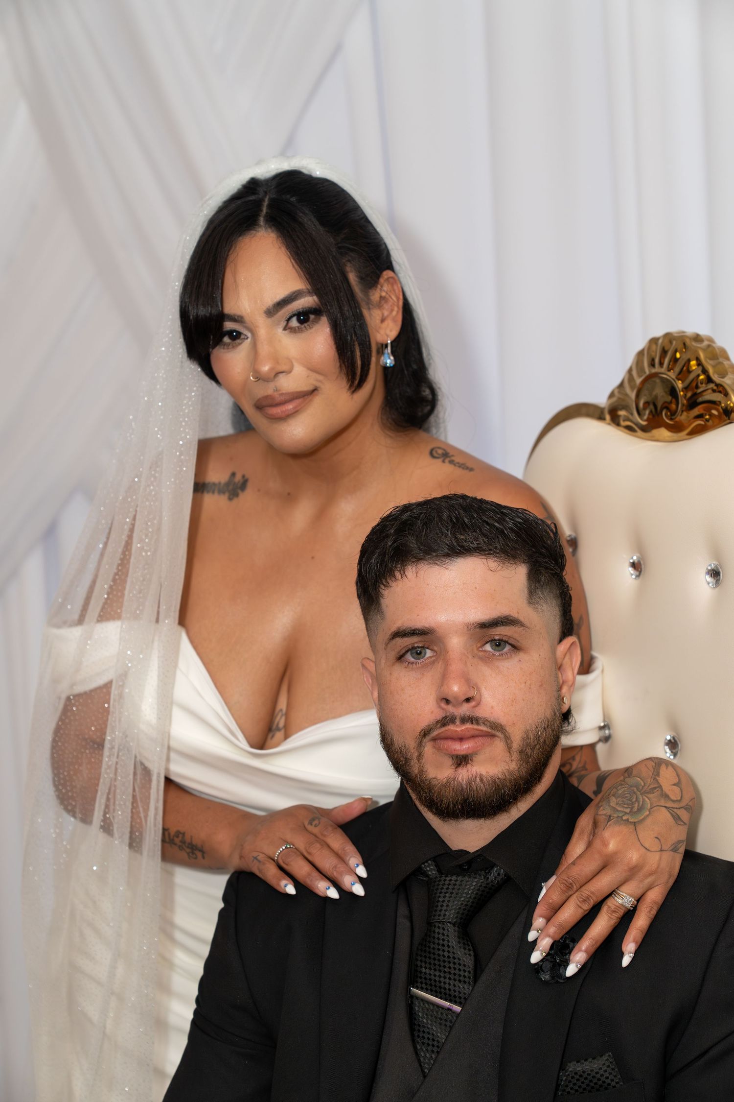 Bride in white gown and veil with groom in black suit posing together at a wedding portrait session.