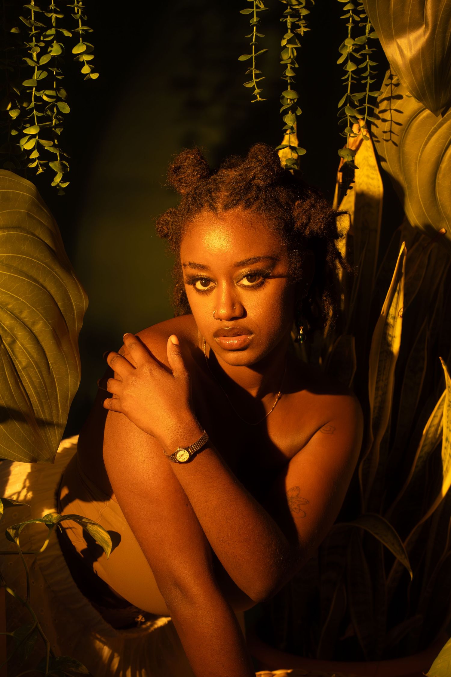 Artistic portrait with warm golden lighting and hanging foliage creating dramatic shadows.