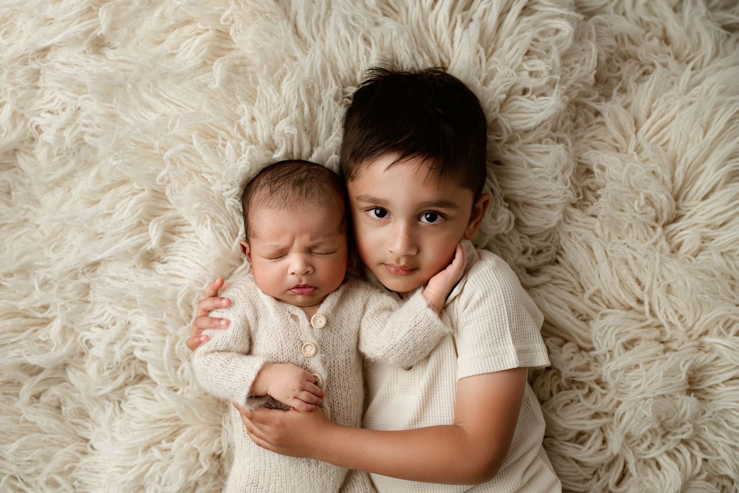 Close-up of a newborn baby lying on a soft cream textured blanket with toddler sibling during a studio photography session