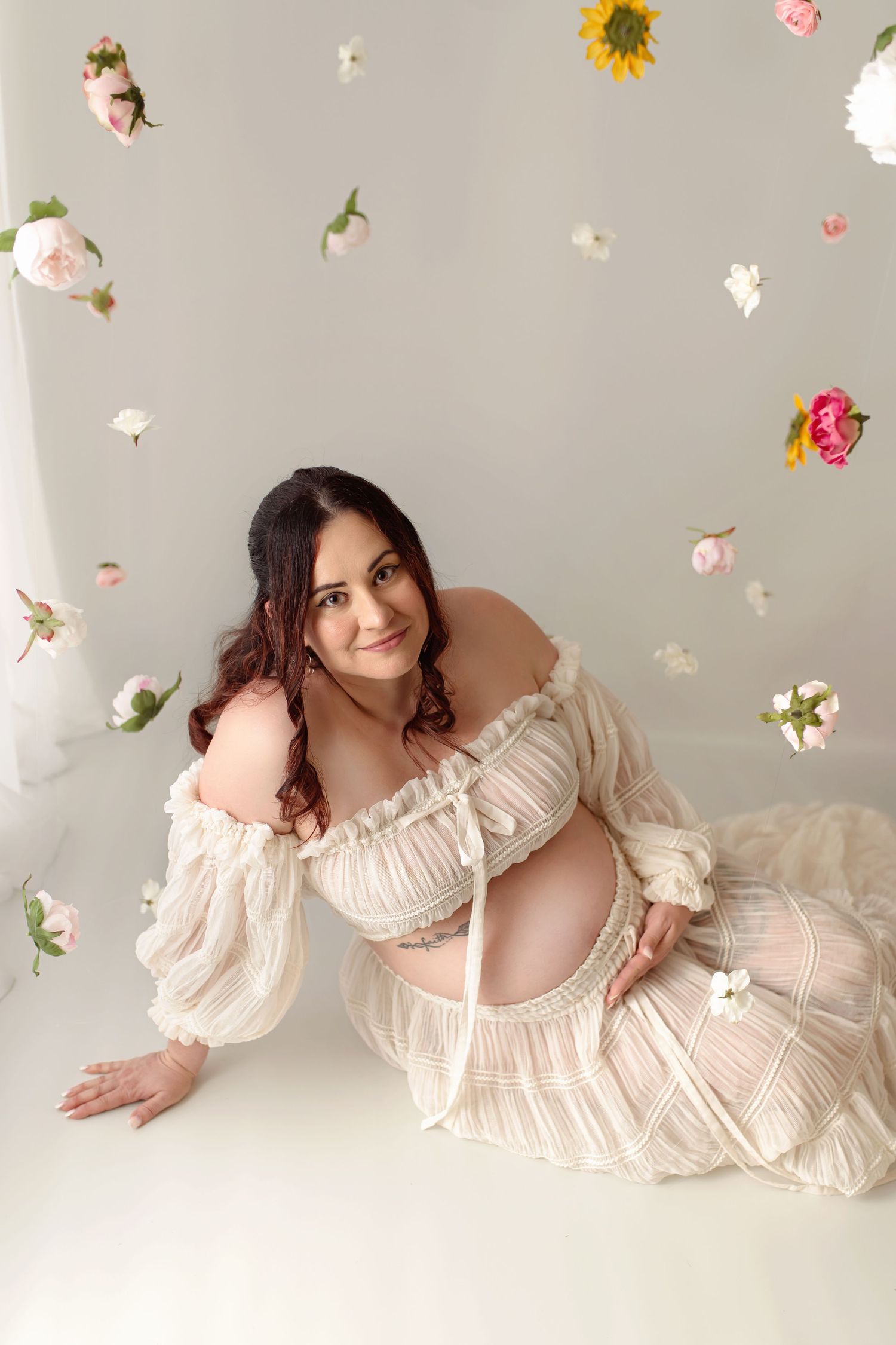 Maternity photography session in Greenville SC featuring a mother-to-be in a flowing cream dress surrounded by flowers.