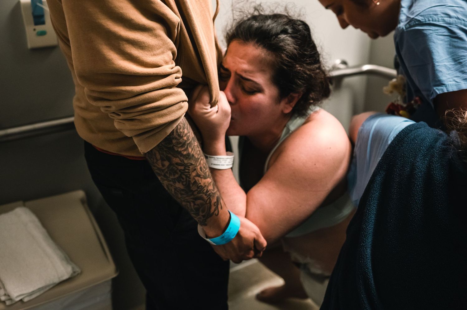 Person in labor holds onto partner's arm during contractions in hospital room.