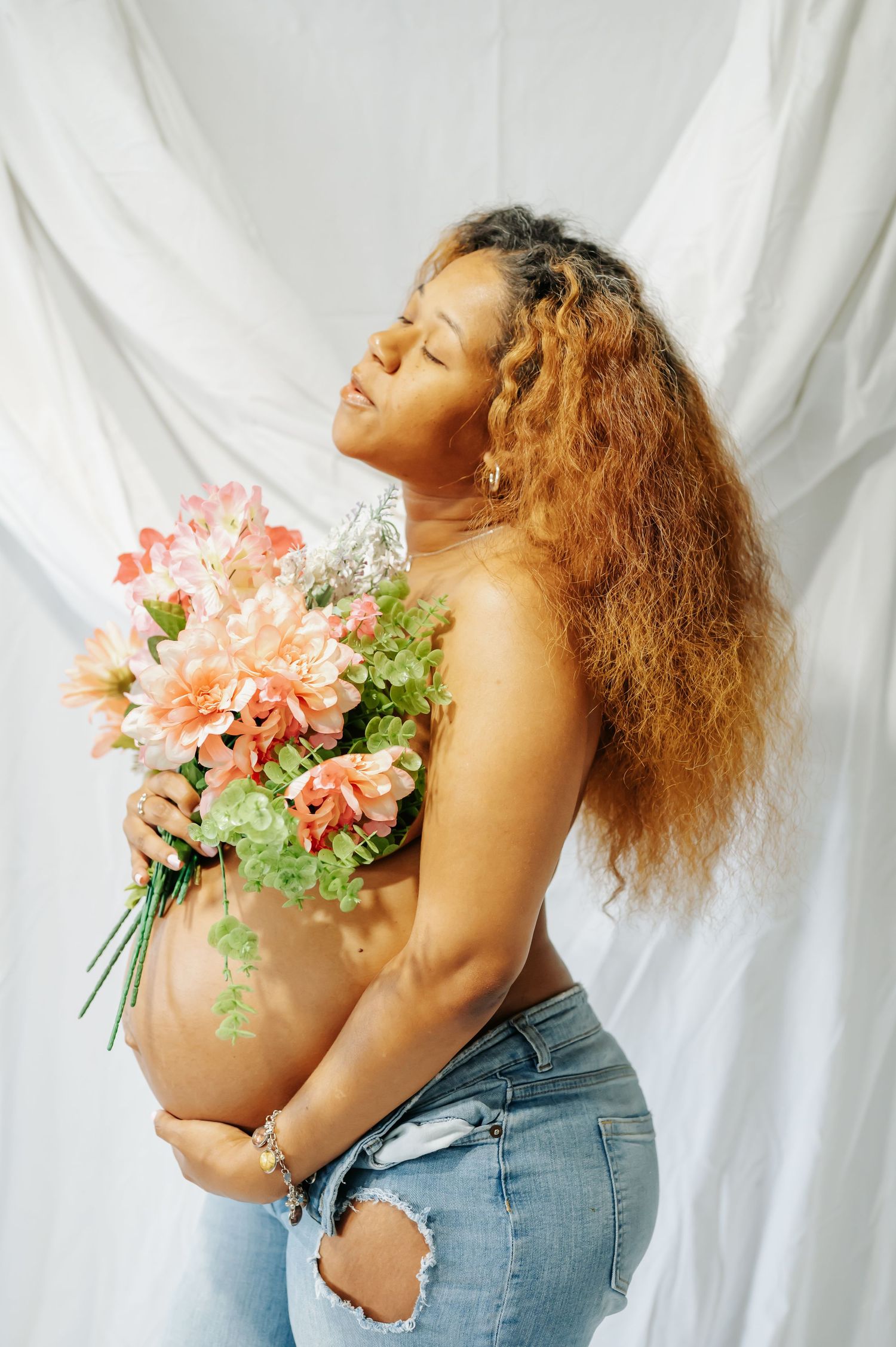 Side view of someone in denim holding pink flowers against white backdrop in artistic photoshoot series.