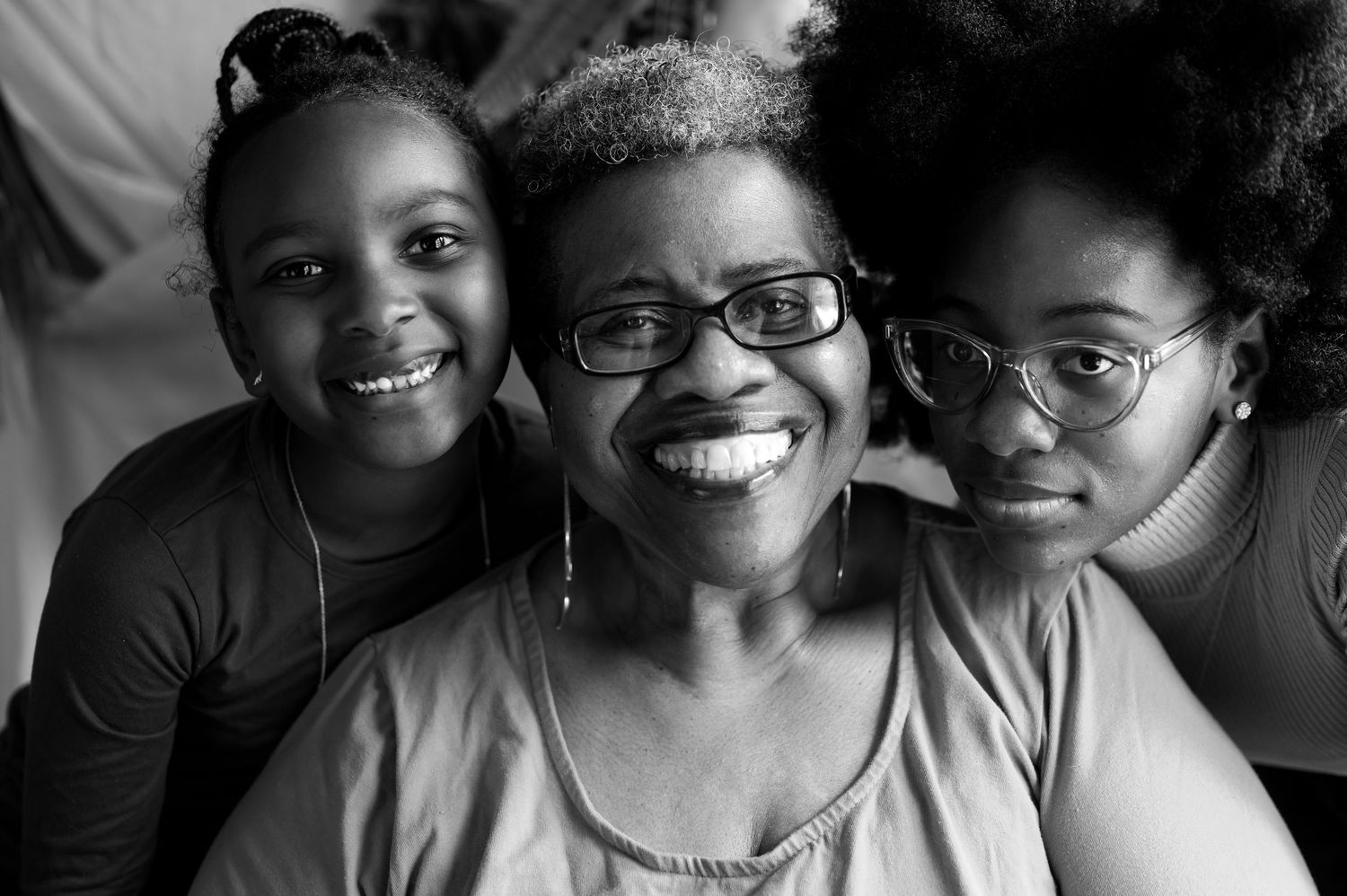 Three smiling Black women pose together in a warm, joyful black-and-white portrait photo.