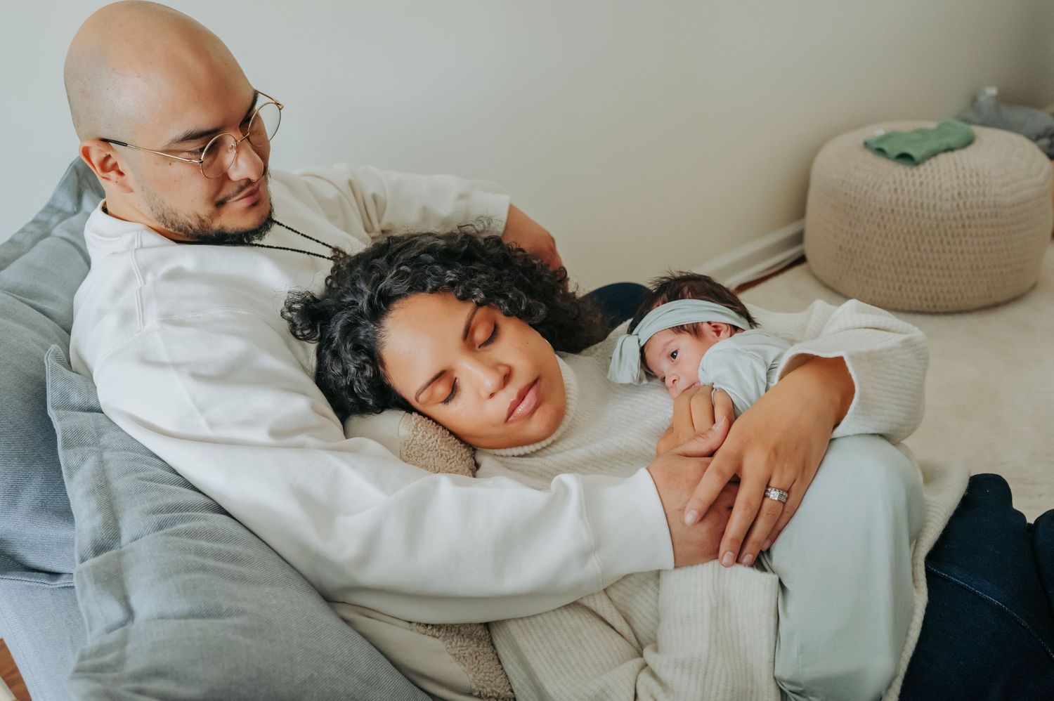 Parents resting together on couch with their newborn baby in a tender family moment.