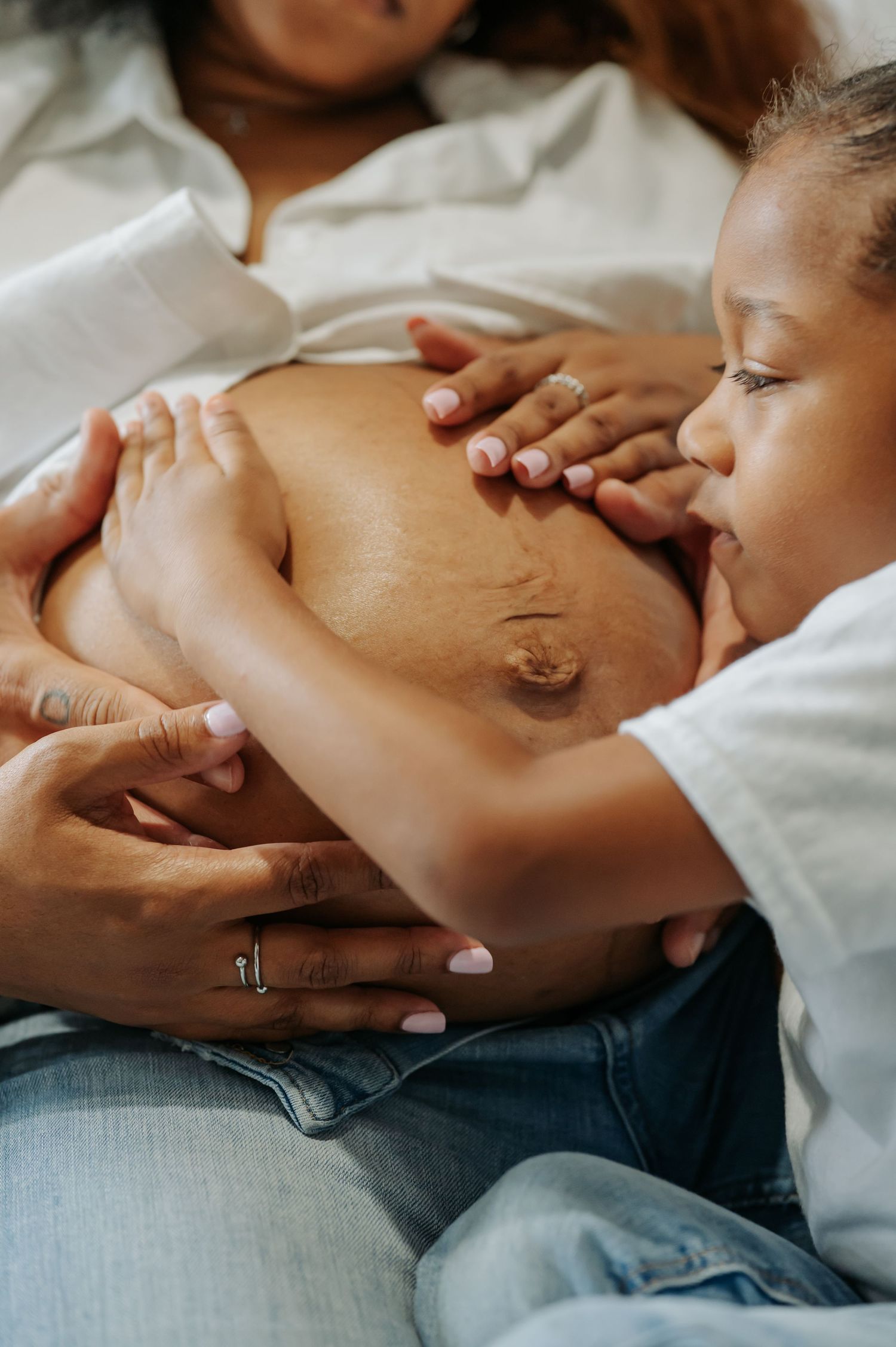 Intimate close-up photo of a pregnant belly being lovingly touched by hands against white bedding.